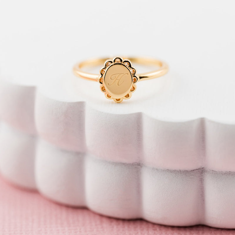 Gold ring with a circular design on a white textured stand with a pink background